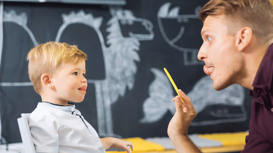 A man demonstrates pencil use to a child, supporting speech therapy through hands-on learning and engagement.