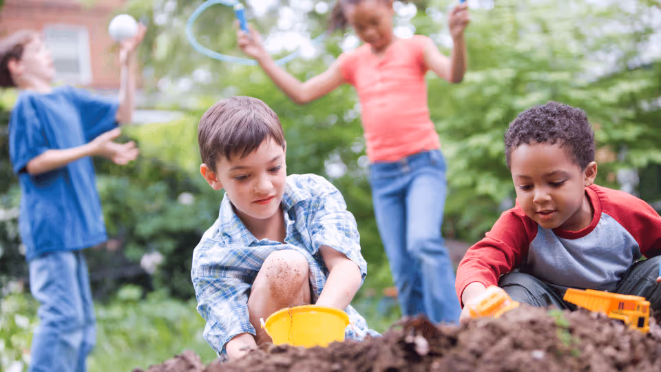 A group of children happily playing in the dirt, using various toys to create and explore their surroundings.
