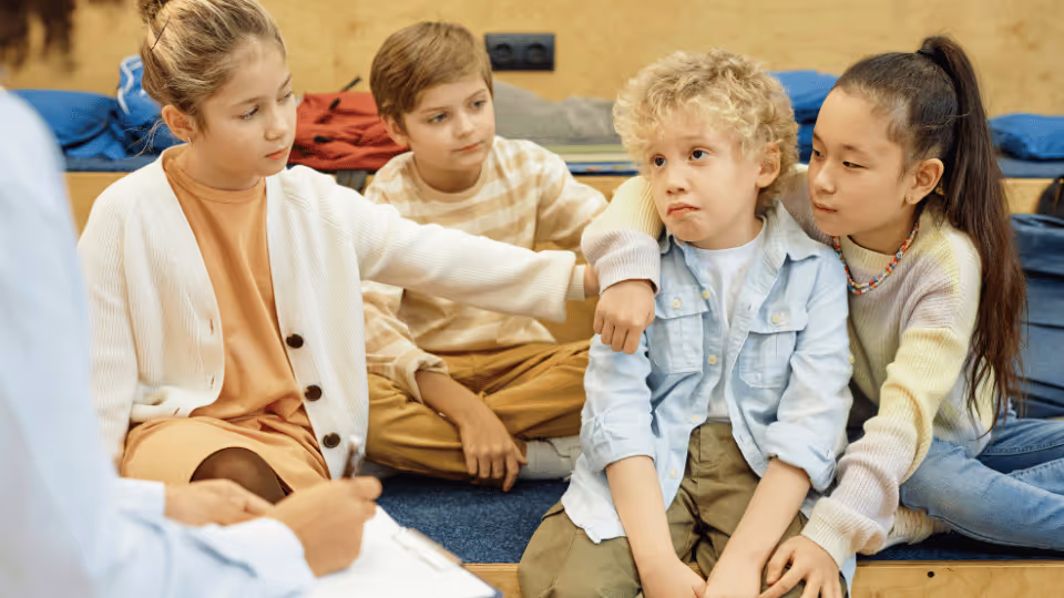 A therapist sits on the floor with a group of children, engaging in activities to support their mental health.