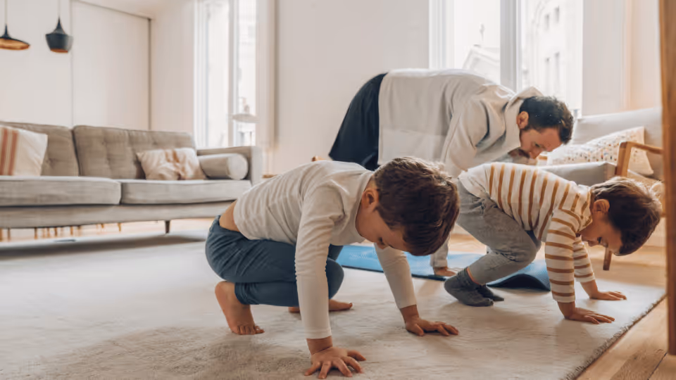 A family of three children engaged in yoga exercises in their living room as part of a physical therapy session.