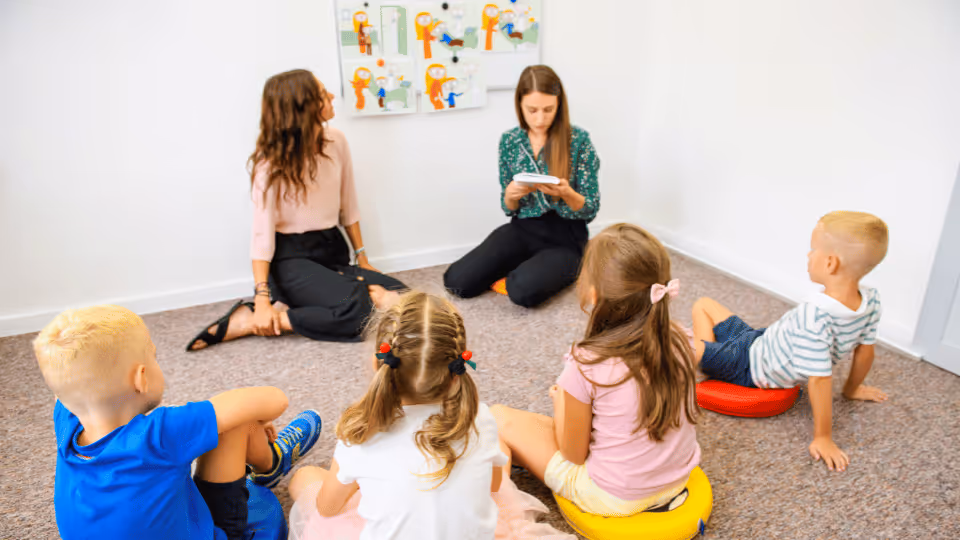 A group of children sitting in a circle on the floor during a physical therapy session led by a therapist.
