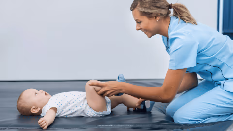 A nurse assists a baby in standing during a physical therapy session, promoting the child's mobility and strength development.