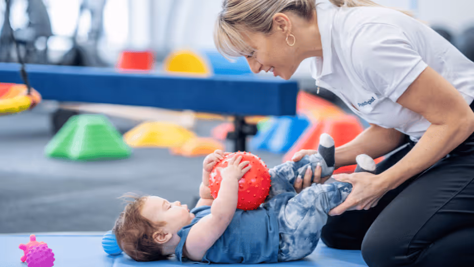 A physical therapist assists a baby in playing with a ball during a therapy session, promoting motor skills development.