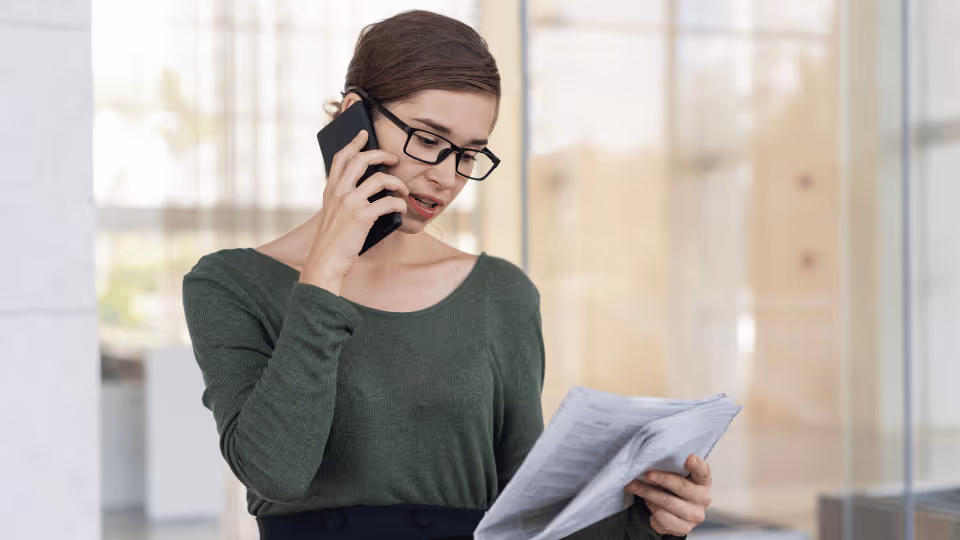 A physical therapist in a green shirt and glasses engages in a phone conversation while assisting a client.