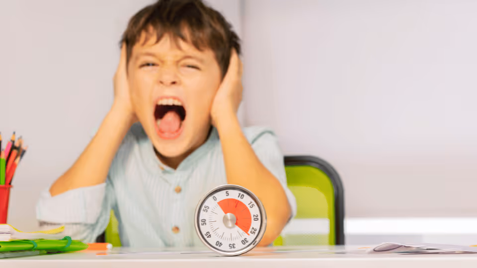 In a child therapy session, a boy is seated at a desk, observing an alarm clock as part of the therapeutic process.
