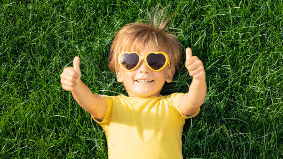A young boy in sunglasses relaxes on the grass during a child therapy session, enjoying a moment of calm and play.