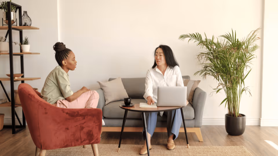 Two women engaged in a child therapy session, seated on a couch in a cozy living room setting.