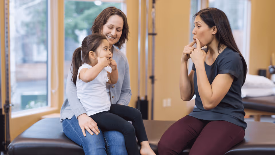 A woman and a child sit on a gym bench during a speech therapy session, focusing on communication and interaction.