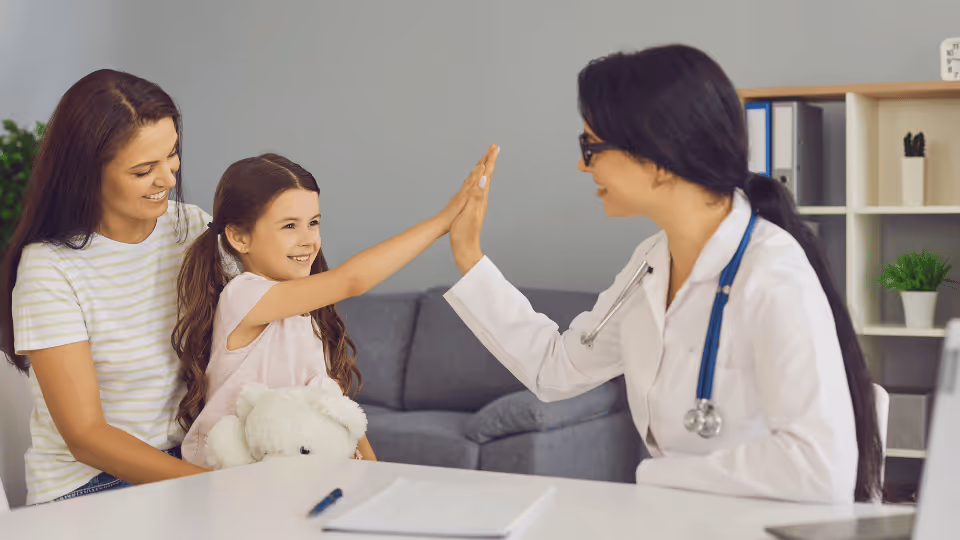 A woman and a child at a desk share a high five with a doctor, highlighting a moment in occupational therapy.