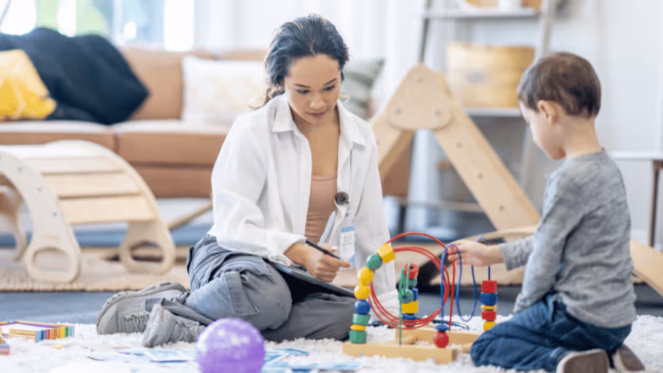 A woman and a child engage in play with toys on the floor, promoting developmental skills through occupational therapy.