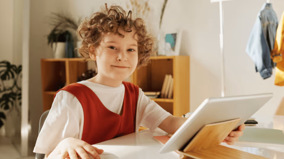 A young boy seated at a table, focused on a tablet while searching for a physical therapist.