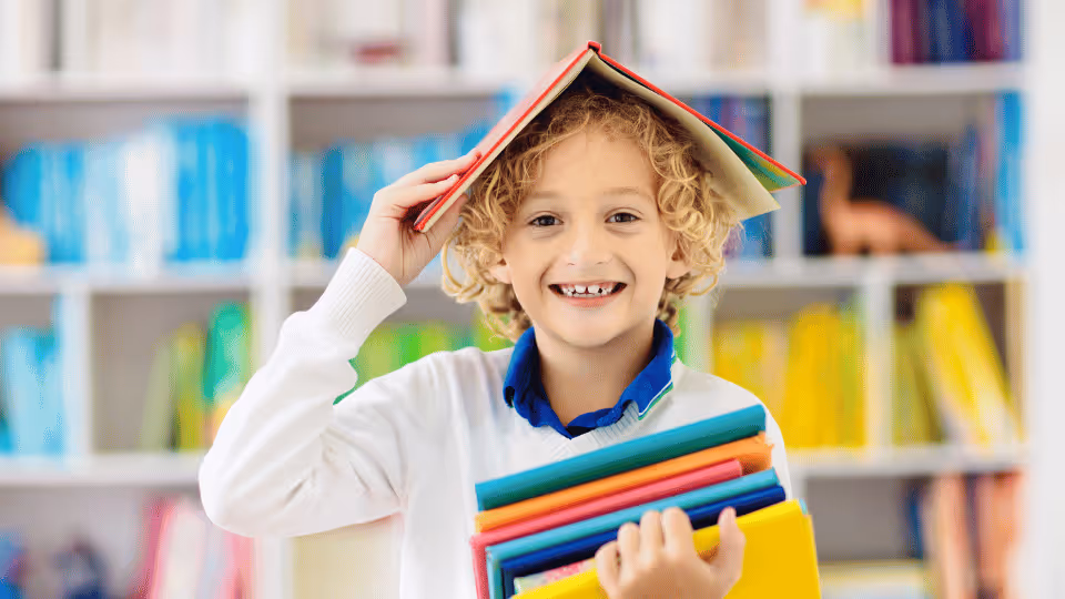 A young boy proudly holds a stack of books, showcasing his enthusiasm for reading and learning.