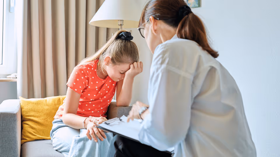 A woman engages in a supportive conversation with a young girl, emphasizing the importance of mental health awareness.