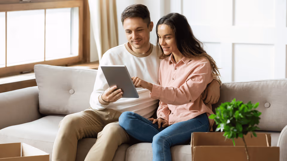 A young couple sits on a couch, engaged with a tablet, discussing how to choose the right pediatric therapist.