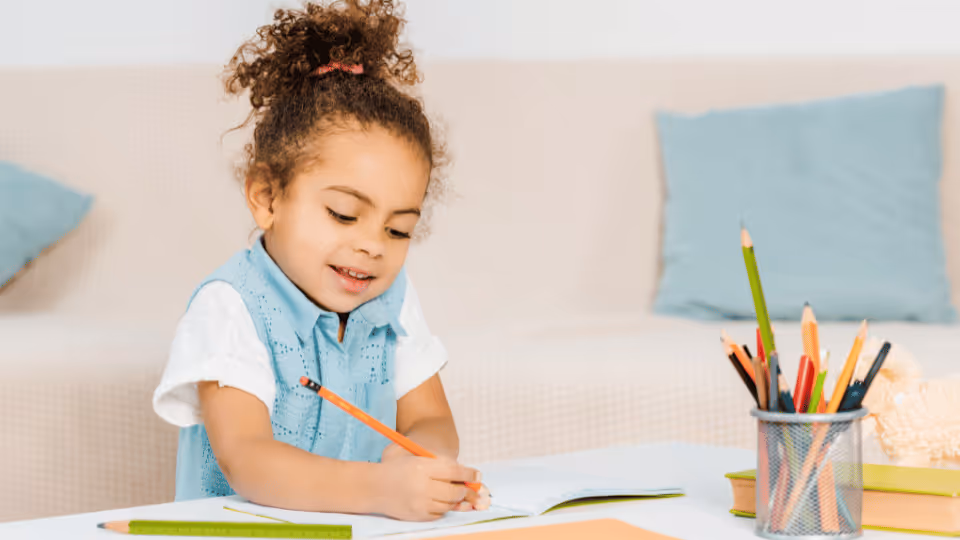 A young girl sits at a table, focused on her notebook and pencil, symbolizing goal-setting in physical therapy.