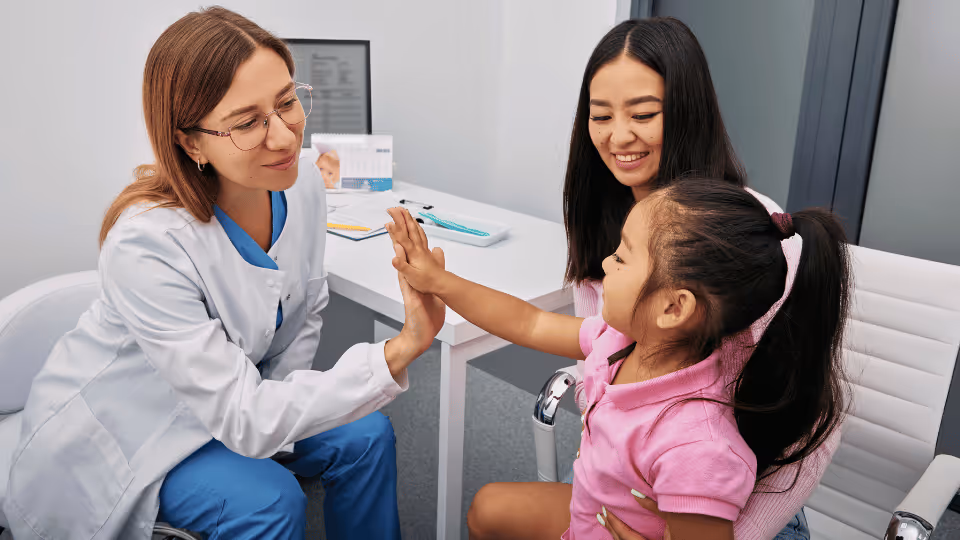 A woman and a young girl sit together in a pediatric therapy doctor's office, awaiting their appointment.