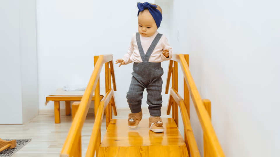 A young girl in overalls ascends a wooden staircase, showcasing her developing motor planning and control skills.