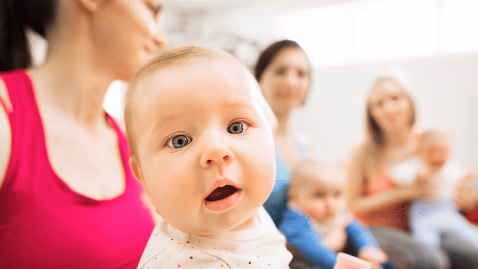 A baby gazes at the camera, accompanied by a woman and two others, highlighting key milestones in fine motor development.