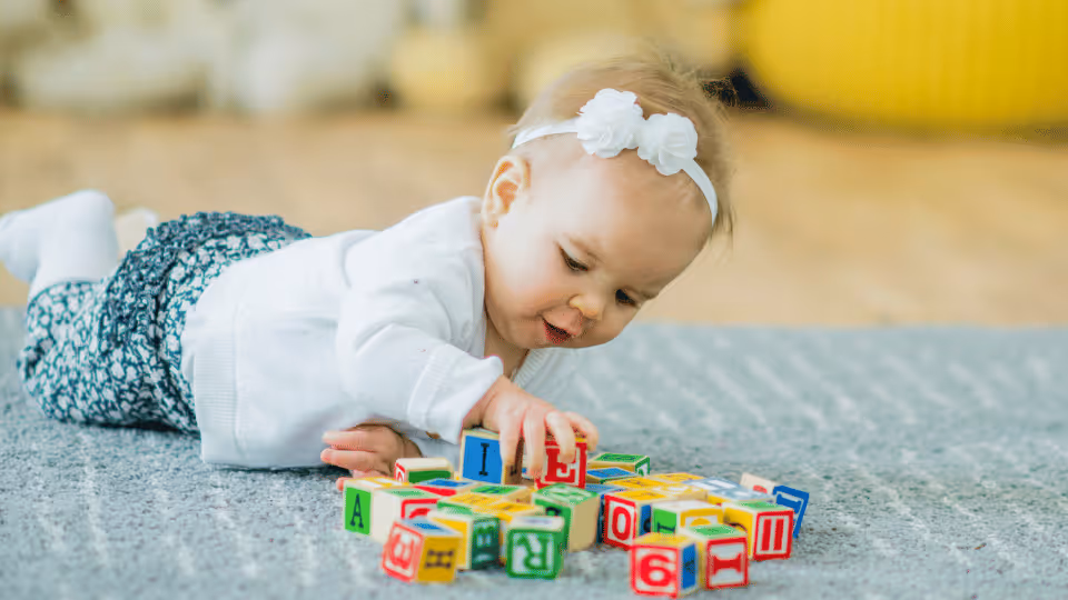 A baby girl engages with colorful blocks on the floor, enhancing her fine motor skills through play.