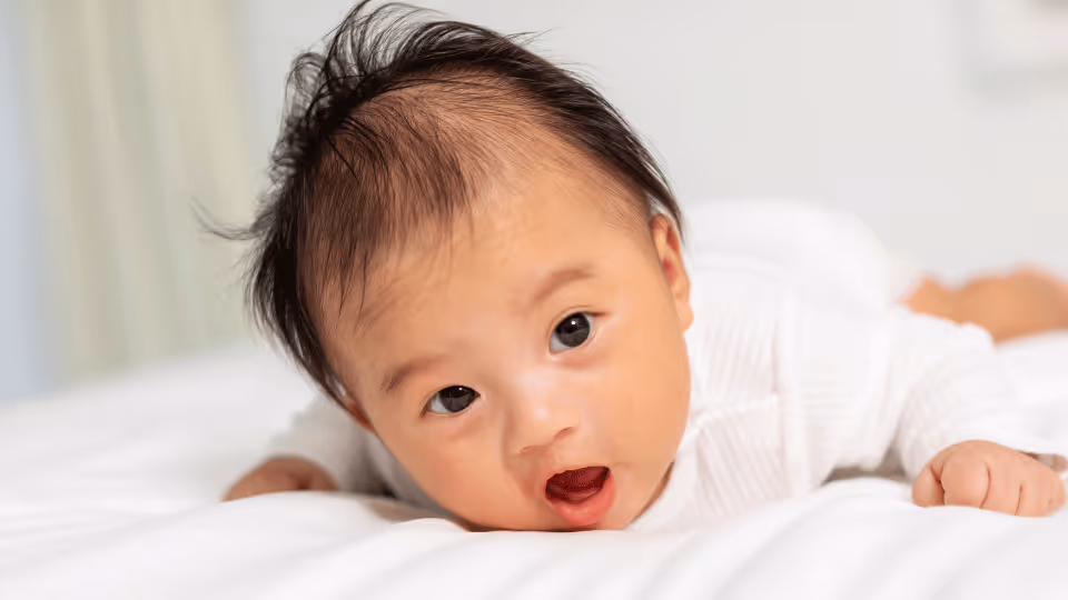 A baby lying on a bed with its mouth open, highlighting the importance of tummy time for infant development.