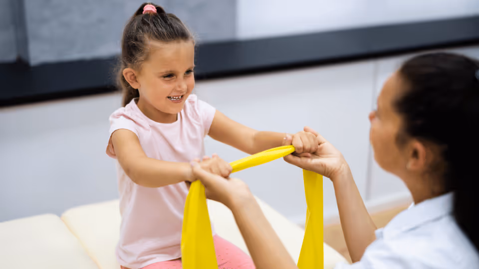 A young girl receives assistance from a physical therapist in a pediatric outpatient therapy setting.