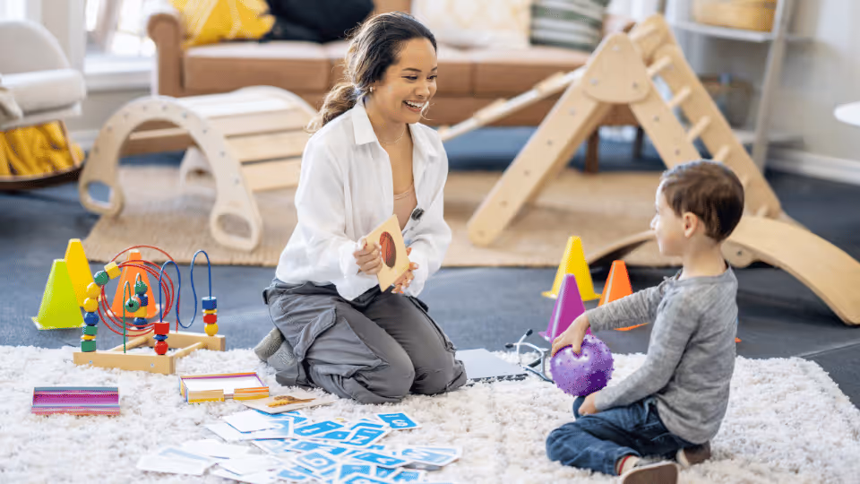 A woman and child engage in playful activities with toys in a bright, cheerful playroom designed for pediatric therapy.