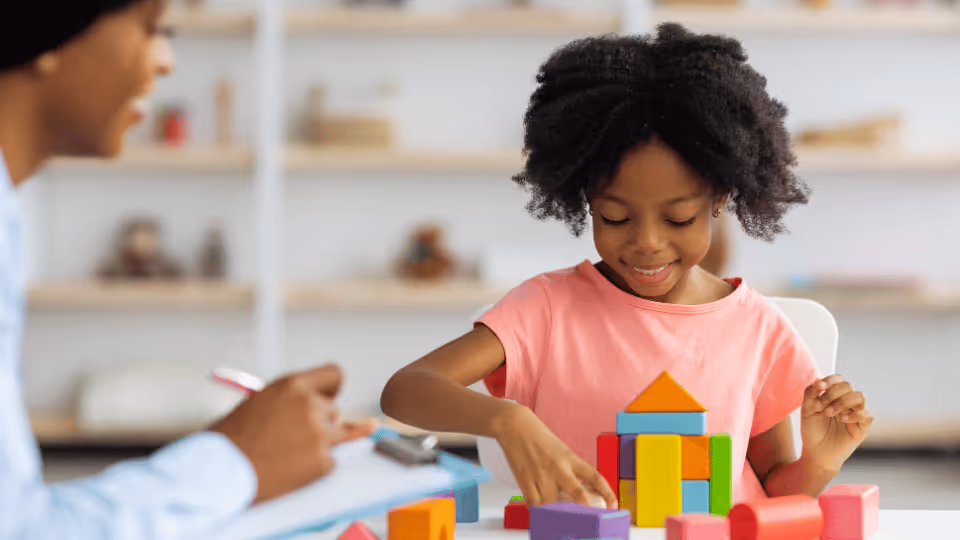 A young girl collaborates with her teacher on building blocks, showcasing the benefits of hands-on learning in rehabilitation.