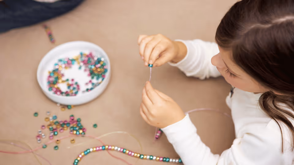A young girl crafts a colorful bead necklace, enhancing her fine motor skills through creative play.