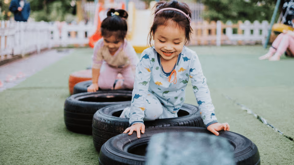 Two young girls enhance their hand-eye coordination while playing on tires in a vibrant playground setting.