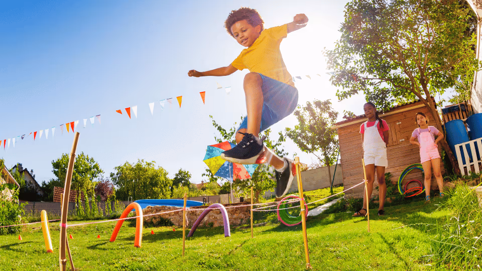 A boy leaps over a backyard fence, showcasing his gross motor skills in action during outdoor play.