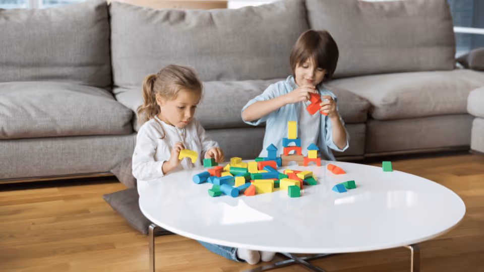 Two children engaged in play, stacking blocks on a table, enhancing their fine motor skills through hands-on activity.