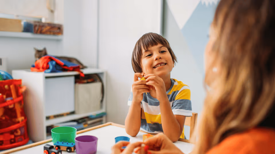 A child and a woman engage in play at a table filled with toys, illustrating effective parent coaching strategies.