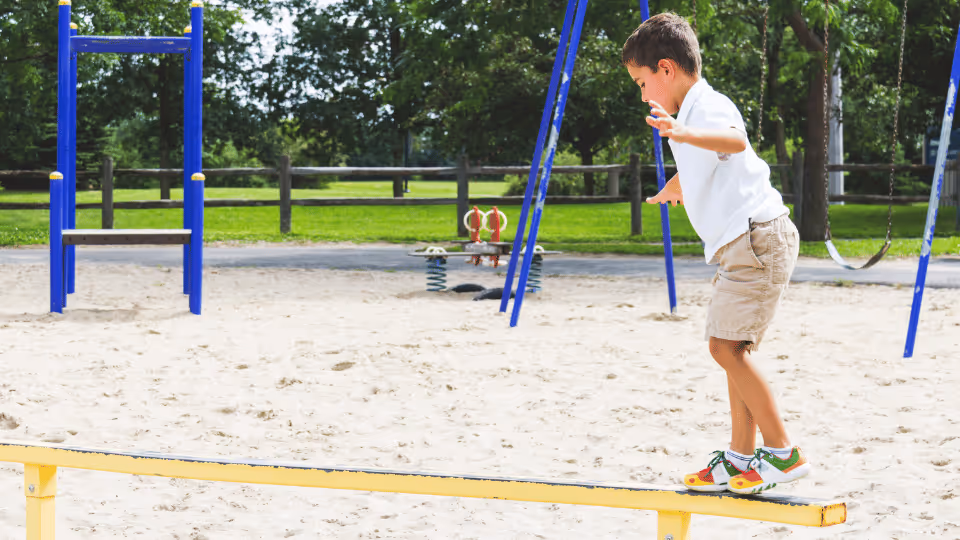 A boy skillfully balances on a rail, showcasing his gross motor skills in a playful outdoor setting.