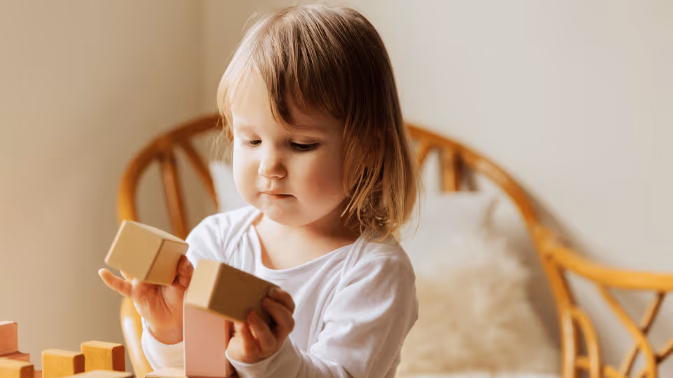 A young girl joyfully stacking wooden blocks, enhancing her fine motor skills through play and creativity.