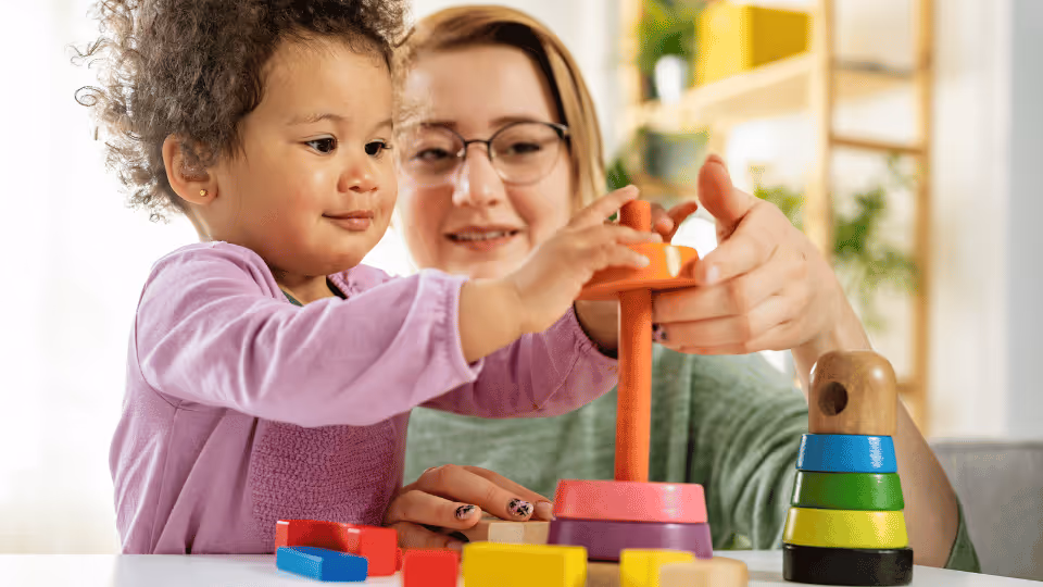 A woman and child engage in play with wooden blocks, fostering creativity and learning in early intervention sessions.