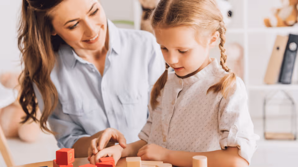 A woman and child engage in play with colorful blocks, promoting developmental skills in pediatric occupational therapy.
