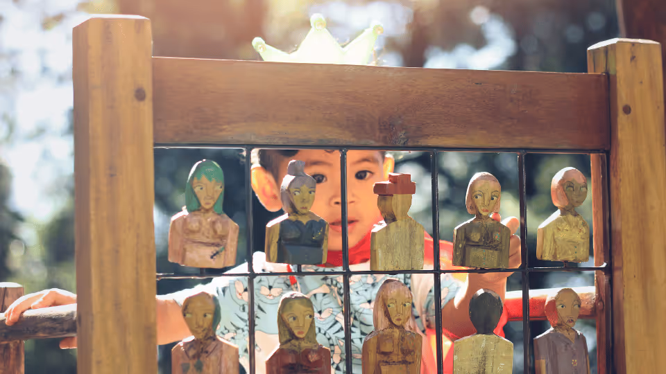 A child stands before a wooden fence adorned with wooden figures, highlighting elements that support gross motor skill development.