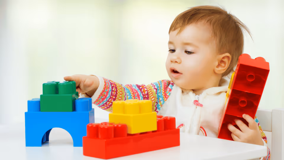 A baby engaged with a toy building set, enhancing gross motor skills through play and exploration.