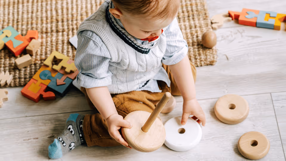 A toddler engages with colorful wooden toys on the floor, enhancing language skills and supporting speech development.