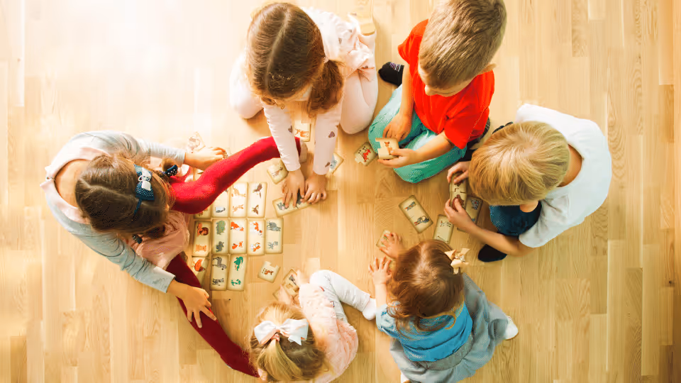 Children engaged in play, assembling wooden blocks on the floor, enhancing their problem-solving skills through verbal cues.