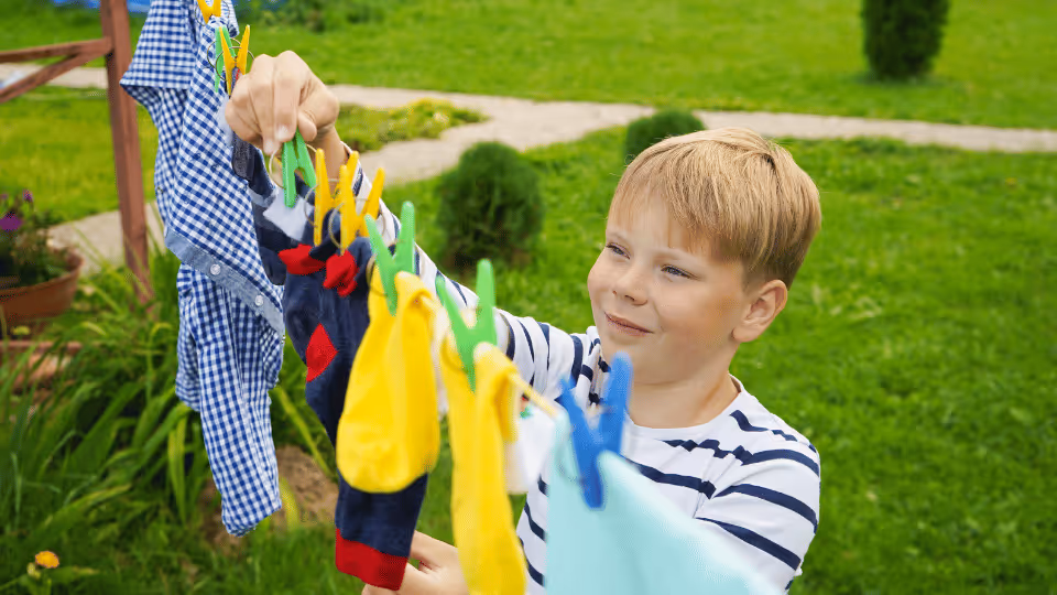 A young boy hangs clothes on a line, engaging in everyday tasks that enhance his fine motor skills.