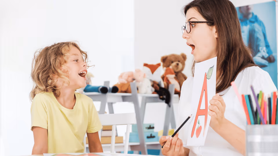 A woman and a child joyfully laugh while holding letters, showcasing the use of visual aids in speech language development.