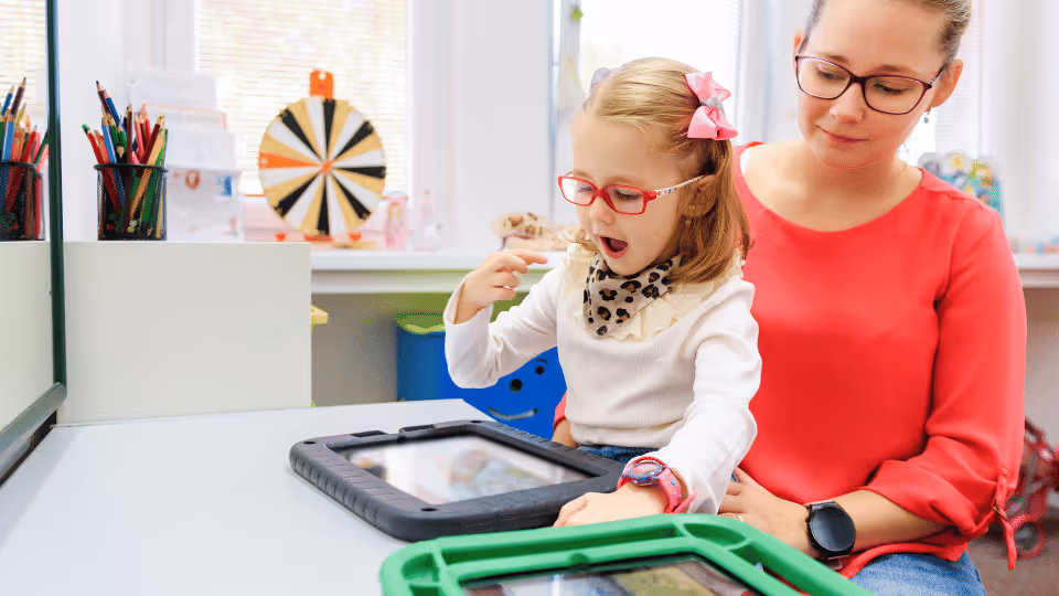 A woman and a young girl engage with a tablet, exploring resources on speech development together