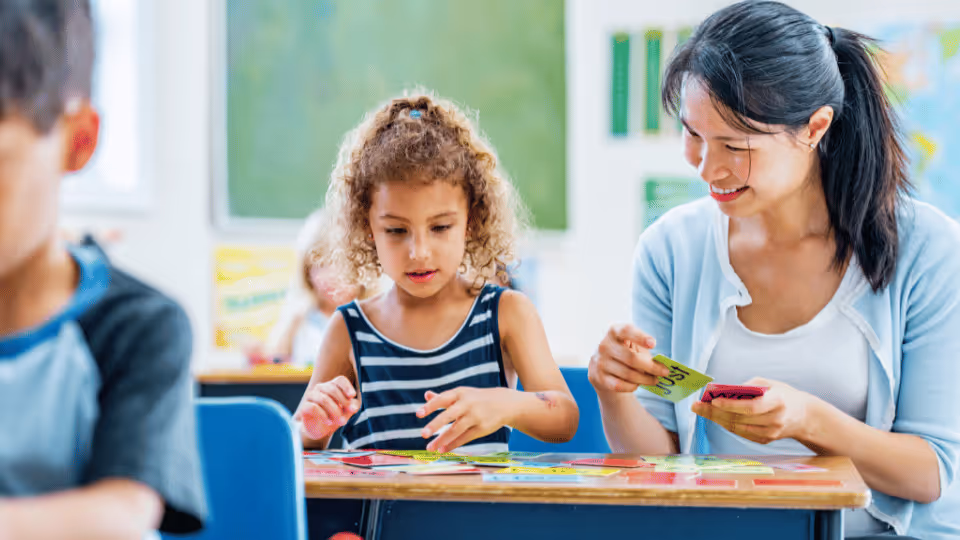 A teacher engages with two children as they collaboratively solve a puzzle, utilizing flashcards and visual aids for learning