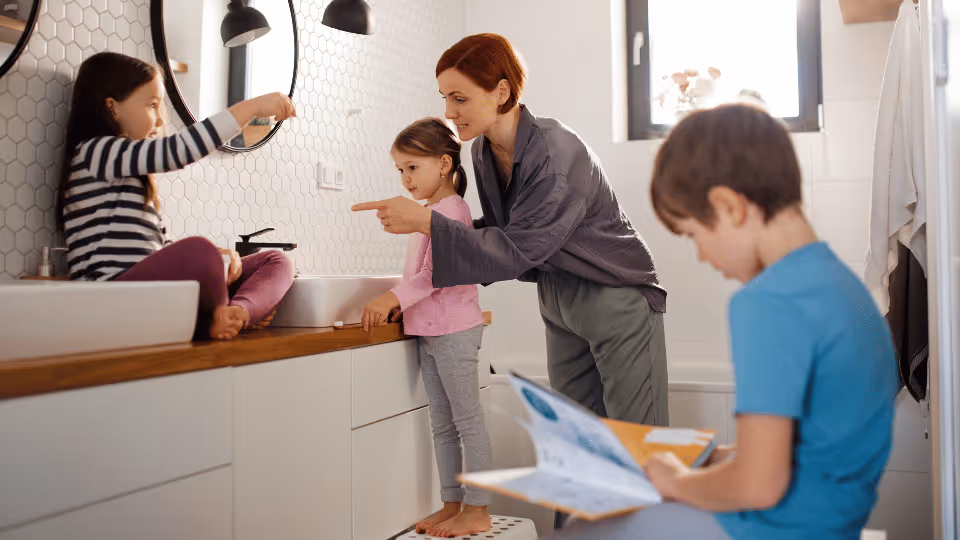 A woman engages with three children in a bathroom, incorporating speech development into their daily routines