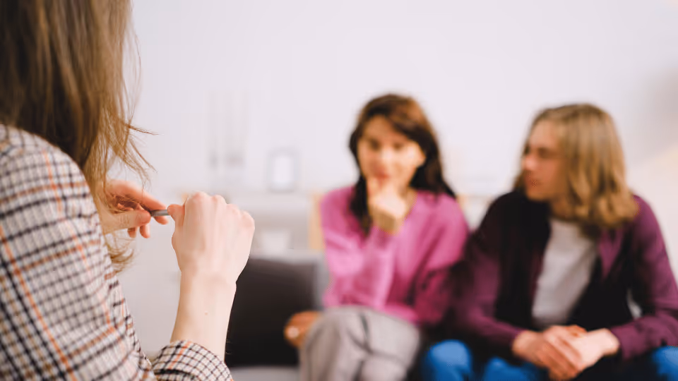 A woman engages in conversation with a man and women during a speech therapy evaluation session