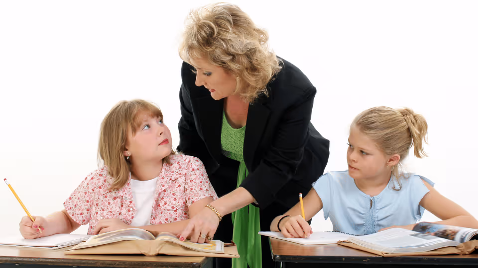 A woman assists two children with homework, fostering their academic growth and addressing emotional and behavioral needs