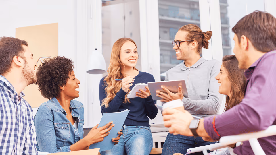 Teachers participating in a professional development meeting, gathered around a table with a tablet for discussion.