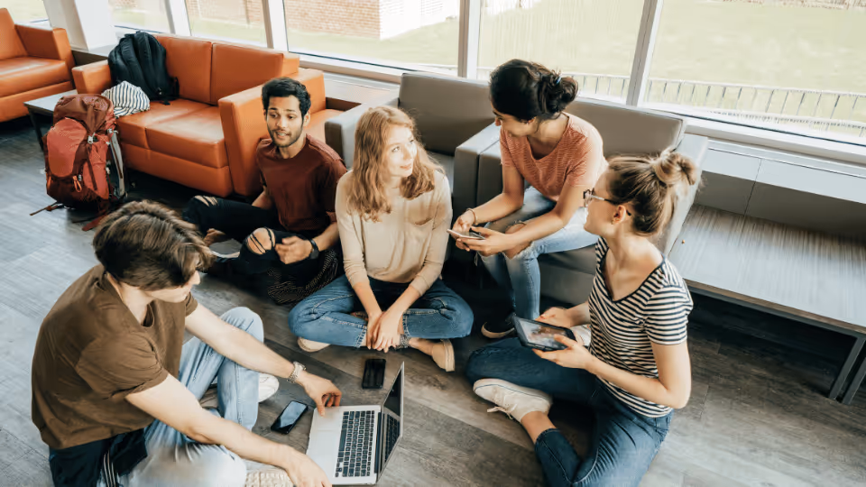 A group of students engaged in conversation while sitting on the floor of a lobby, fostering social skills development.