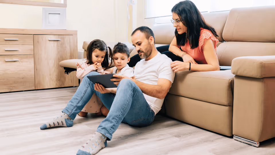 A family on the floor, interacting with a tablet, representing the joint effort of parents and therapists in monitoring development.